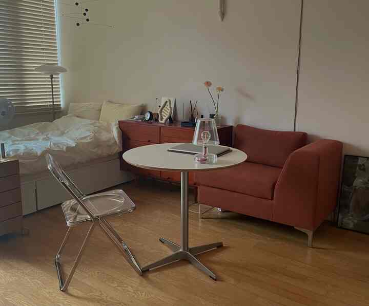 ホワイトとウッドトーンが調和するワンルームの寝室兼リビング、1人用ソファと円形テーブルが配置された落ち着いた空間