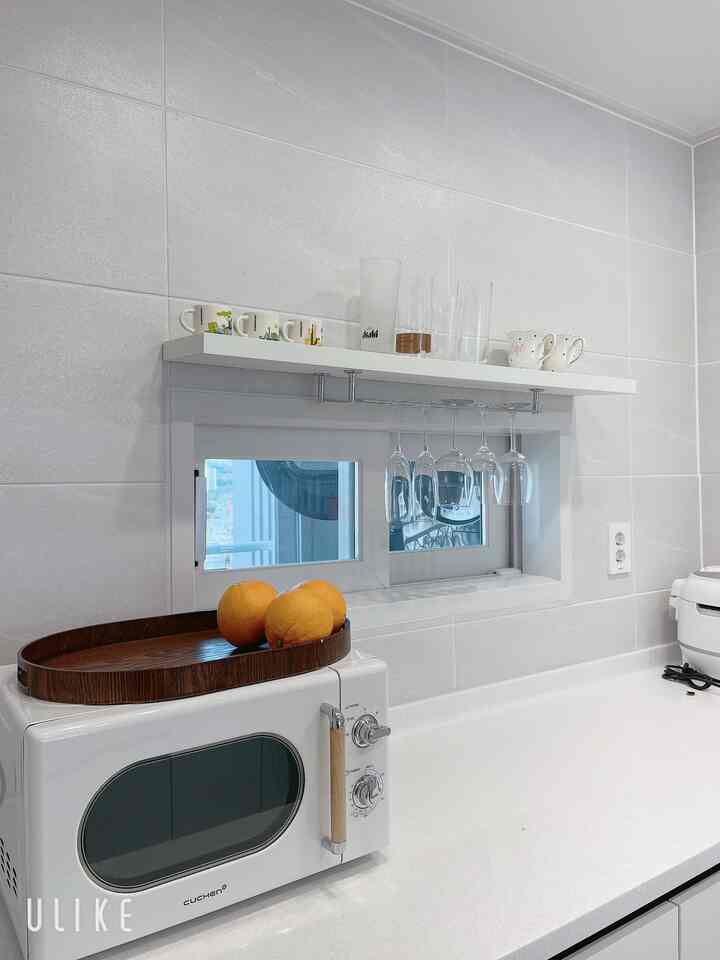 白を基調としたキッチンスペース、レトロな電子レンジとワイングラス、整頓された棚が印象的な空間