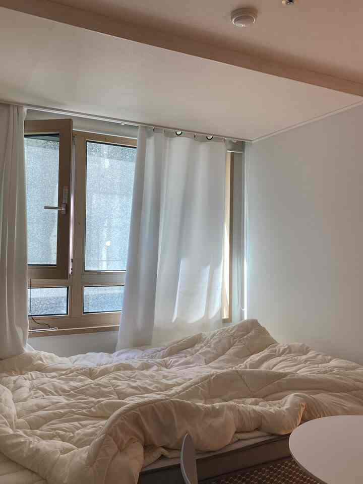 A white and beige toned bedroom featuring a queen-size bed and blackout curtains with a cozy, clean atmosphere