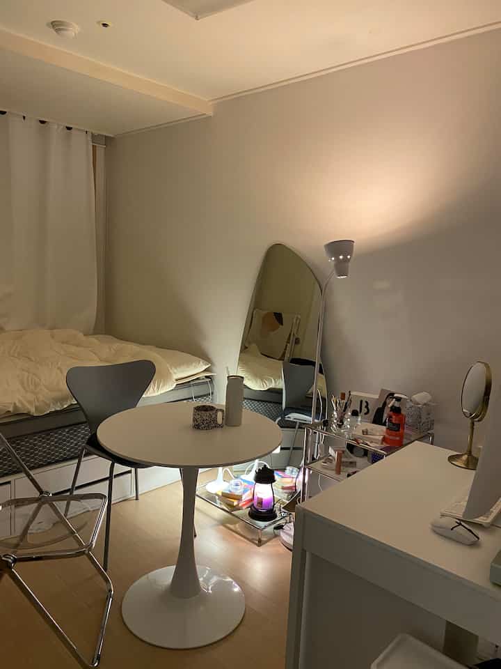 Small bedroom with white and transparent tones featuring a round table and simple furniture creating a warm atmosphere