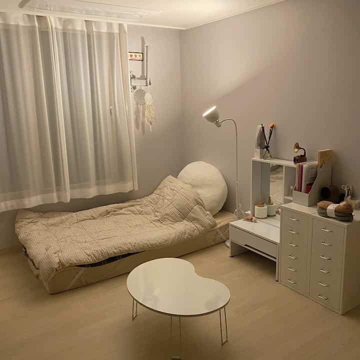 White and beige toned studio bedroom featuring a simple bed and dresser creating a cozy atmosphere