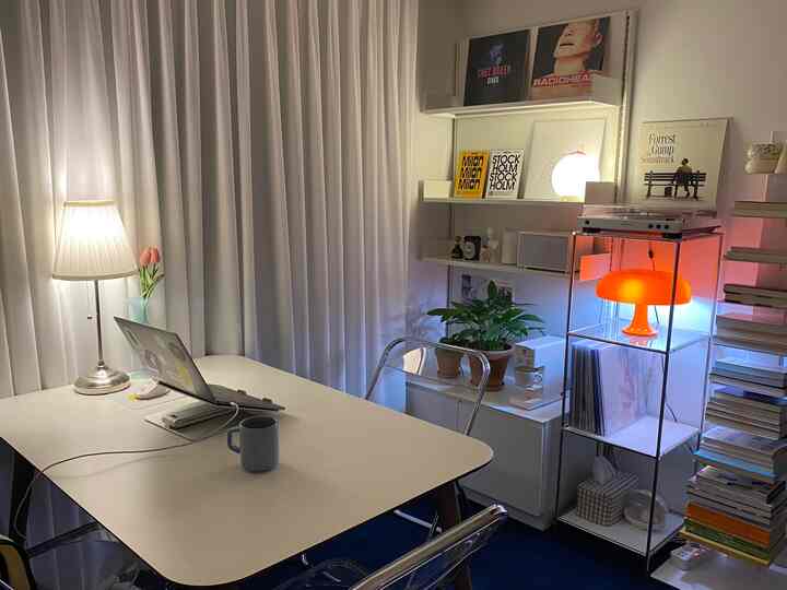 White and blue toned home office space featuring a white desk, transparent chairs, shelves with retro LP records and an orange lamp creating a cozy atmosphere