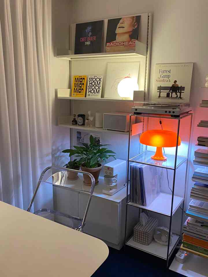 白と透明の色調のリビング、透明の椅子とオレンジのテーブルランプ、植物が配置された落ち着いたレトロな雰囲気のインテリア