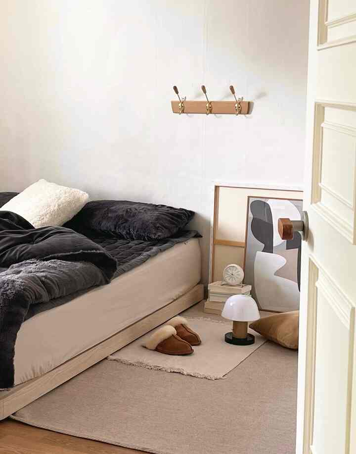 ベージュの色調の寝室、ロータイプベッドと枕、抽象画の額縁が配置されたナチュラルモダンな雰囲気のインテリア