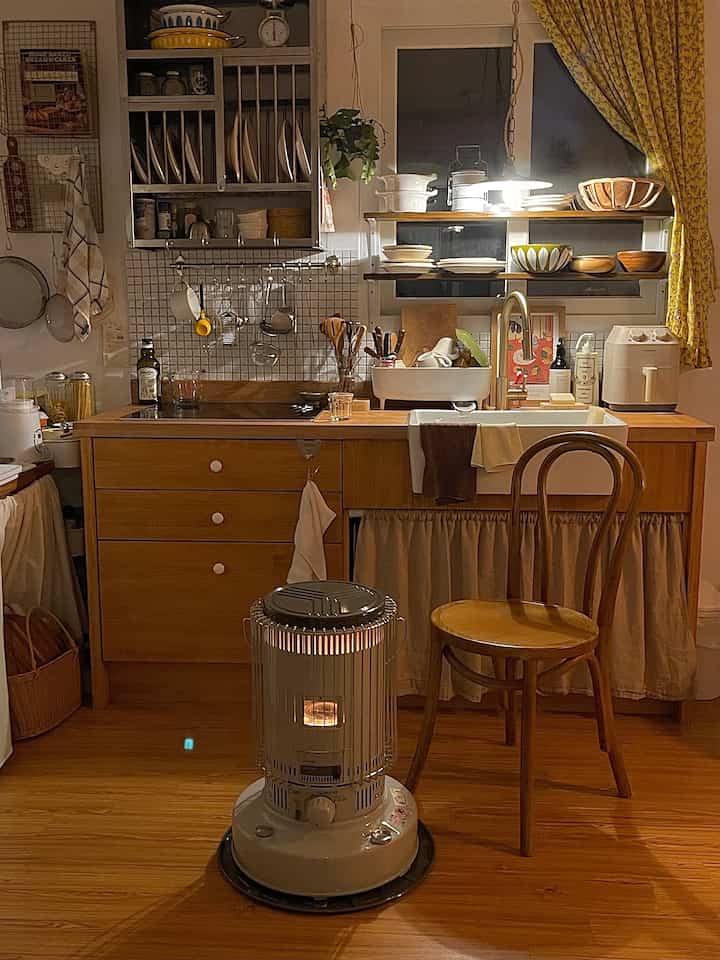 A warm and cozy kitchen featuring brown wood furniture and yellow floral curtains, accented with classic kitchenware and an analog heater