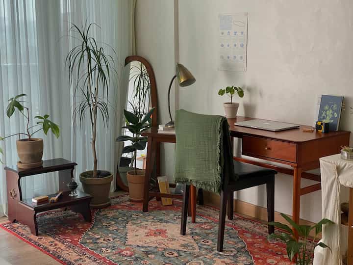 A natural-feeling home office with warm wood tones and vintage rug, featuring plants and a large mirror for a cozy atmosphere
