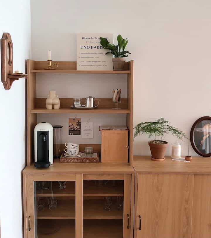 Natural-toned kitchen space featuring wooden cabinets, a Nespresso coffee machine, various objets, and plants creating a cozy atmosphere