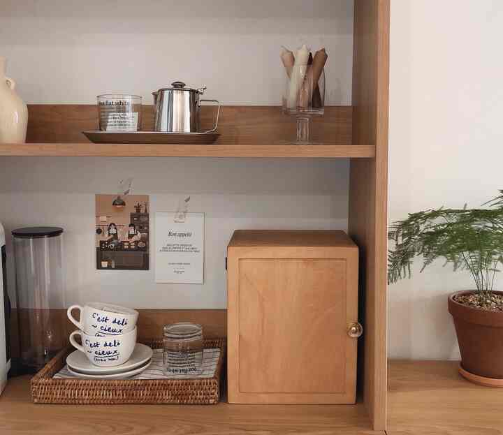 Wood tone and white wall kitchen shelves featuring coffee cups, tray, plant, and candles in a natural, simple space