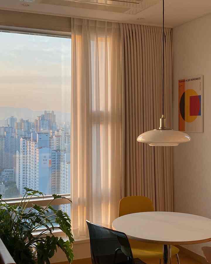 温かみのある白と黄色のトーンのダイニング、カーテンとペンダントライトが配置された雰囲気のあるインテリア