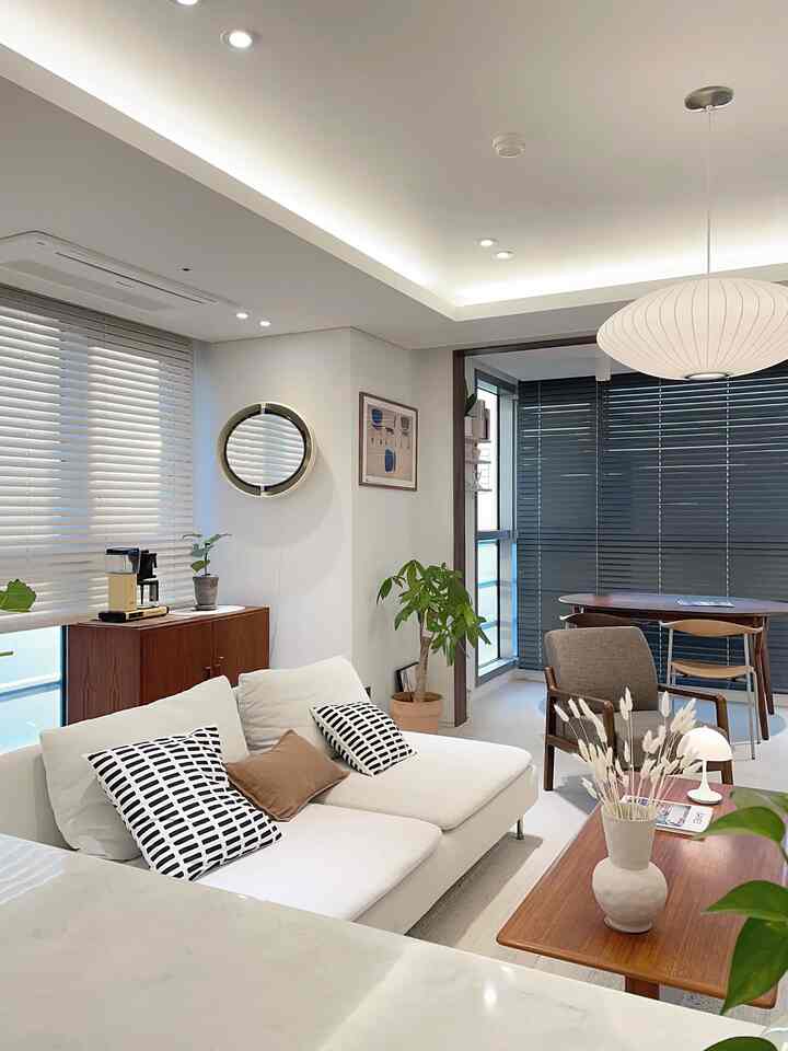 A cozy living and dining area in white and wood tones featuring a mid-century modern sofa, armchair, and a pendant light