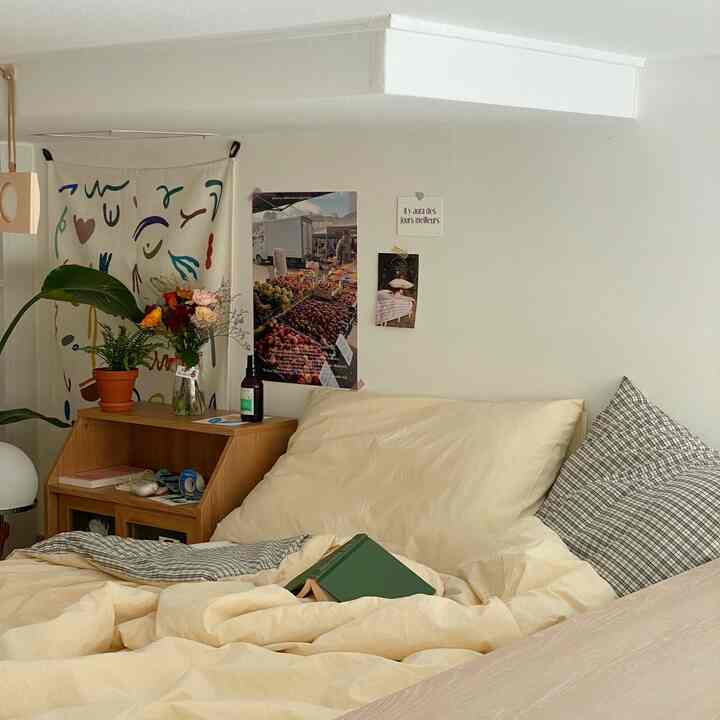 Cozy bedroom with beige bedding and natural wood desk, featuring plants in a warm neutral tone