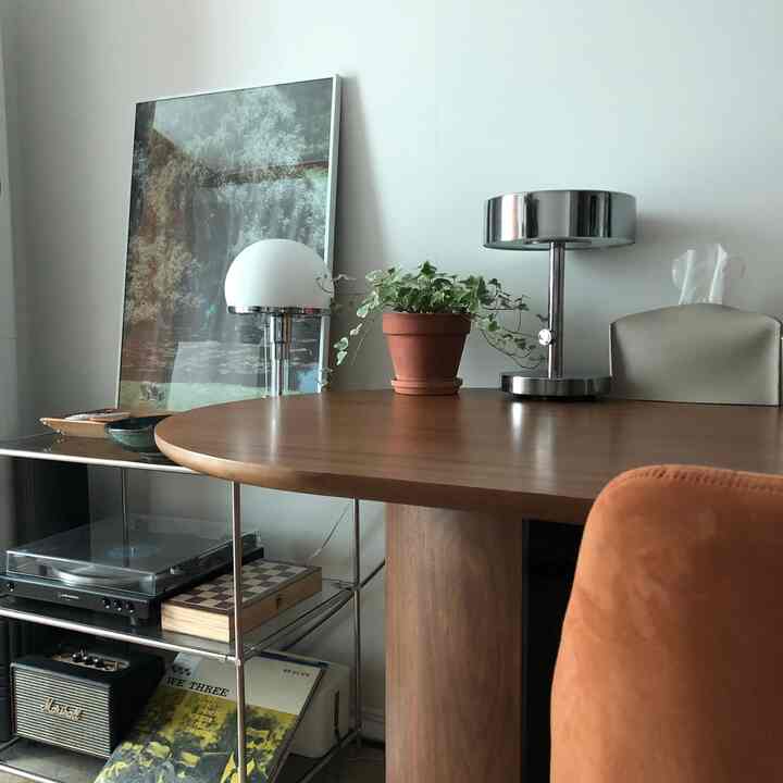 木目調のラウンドダイニングテーブルがあるリビング、テーブル上のスタンドランプとアイビーが配置されたモダンなインテリア