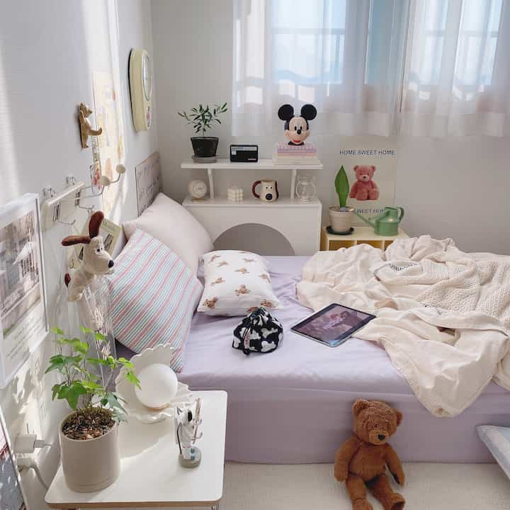 パステル調のワンルーム寝室、かわいいぬいぐるみやクッション、ポスターが配置された居心地の良い空間