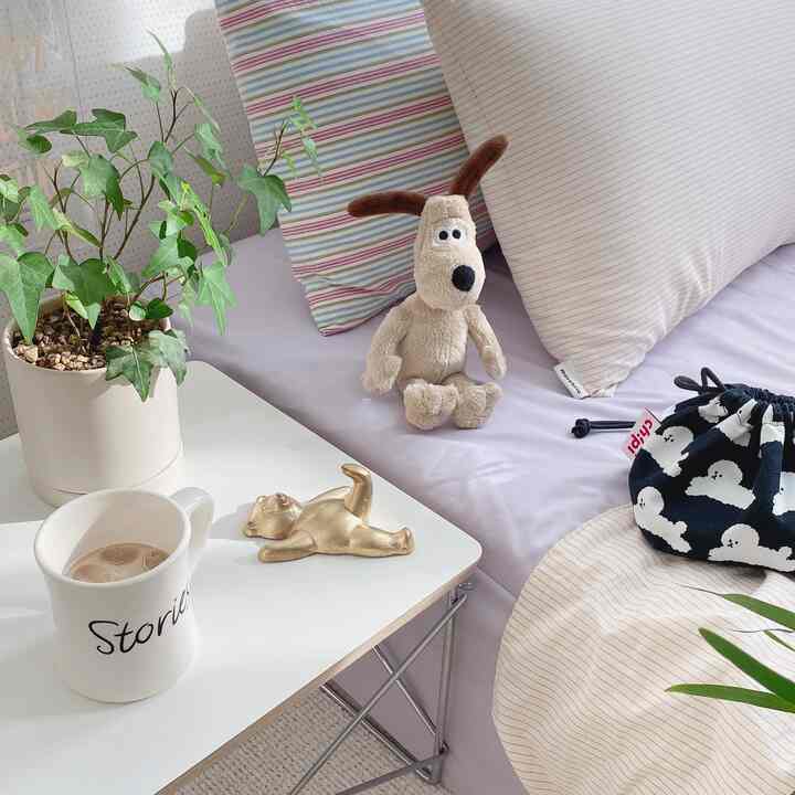White and brown toned bedroom featuring striped bedding, dog plush toy, side table with plant and mug creating cozy atmosphere