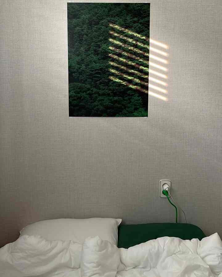 Beige-toned bedroom with white bedding featuring a green forest poster, creating a natural and calm atmosphere