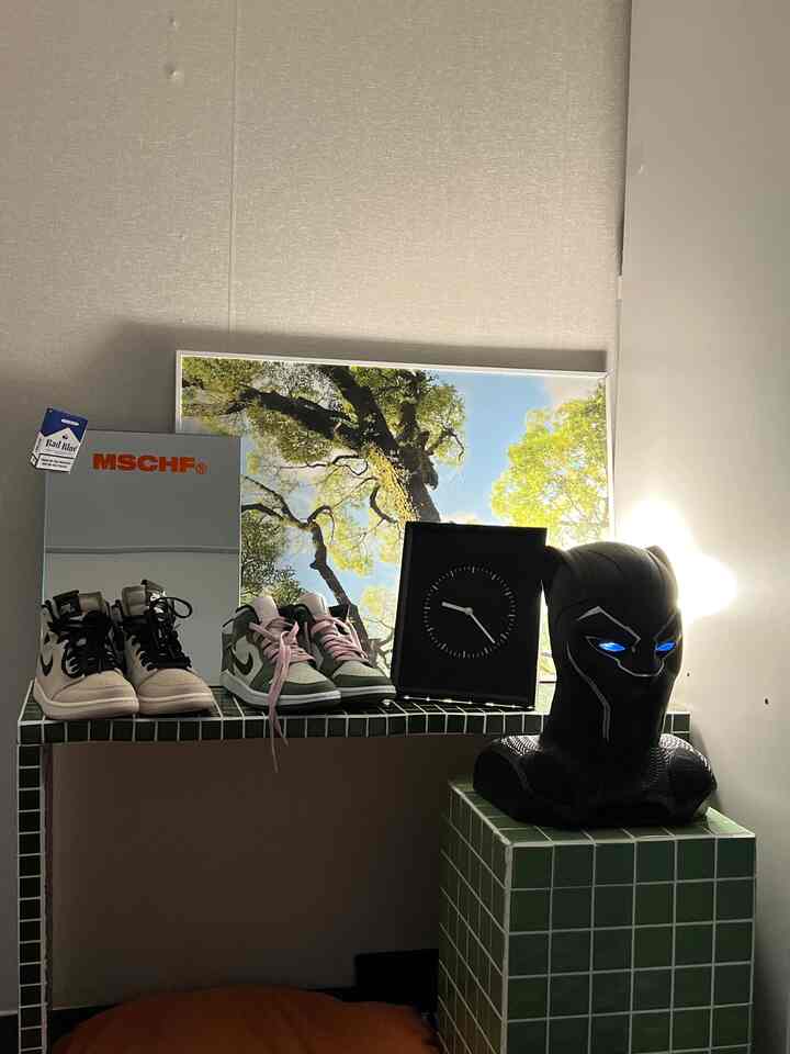 緑のタイル棚に置かれた置き時計とスニーカー二足、木の絵が飾られた雰囲気のあるインテリア