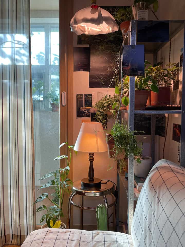 暖かいベージュとナチュラルトーンのリビングの一角、スツール上のライトと植物が調和した雰囲気のあるインテリア