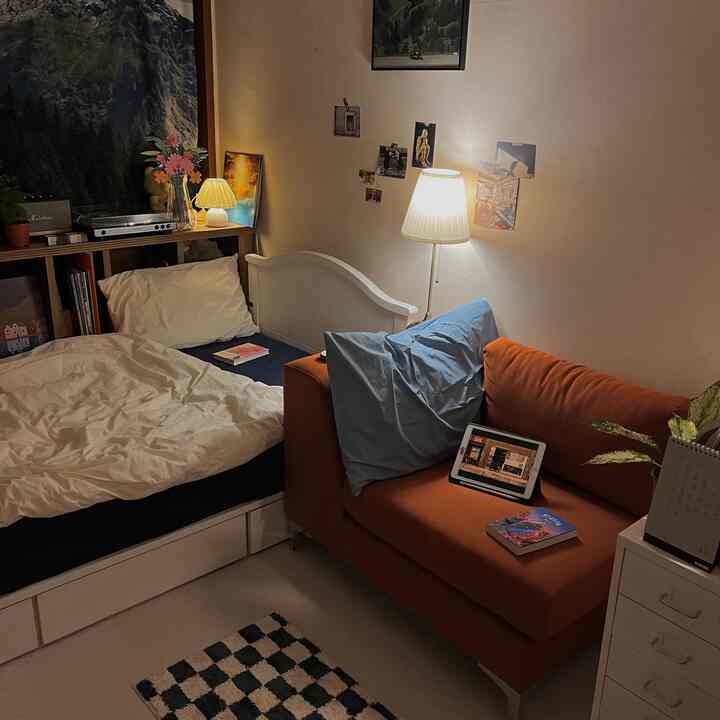 暖かいベージュとオレンジのトーンの小さな寝室、一人用ベッドとオレンジ色のソファが配置された居心地の良い空間