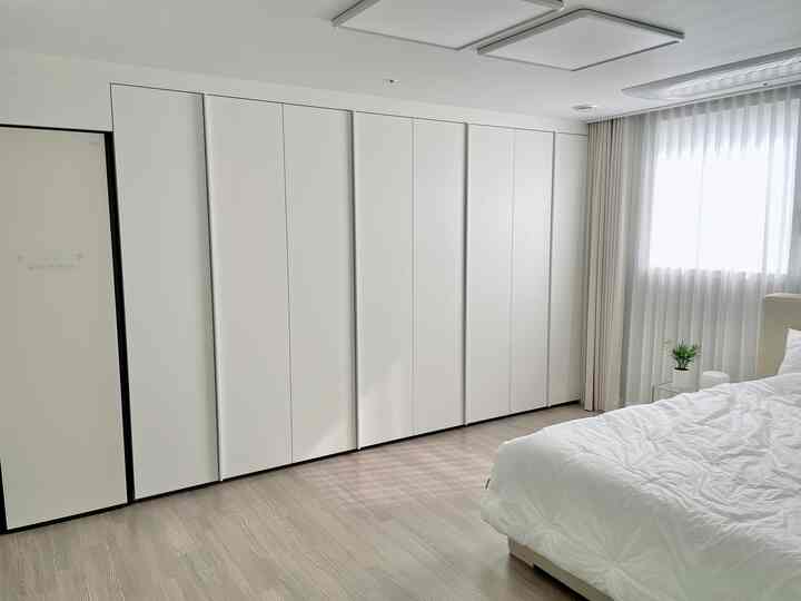 白とナチュラルトーンの寝室、クローゼットとベッドが配置された清潔感のある明るいインテリア