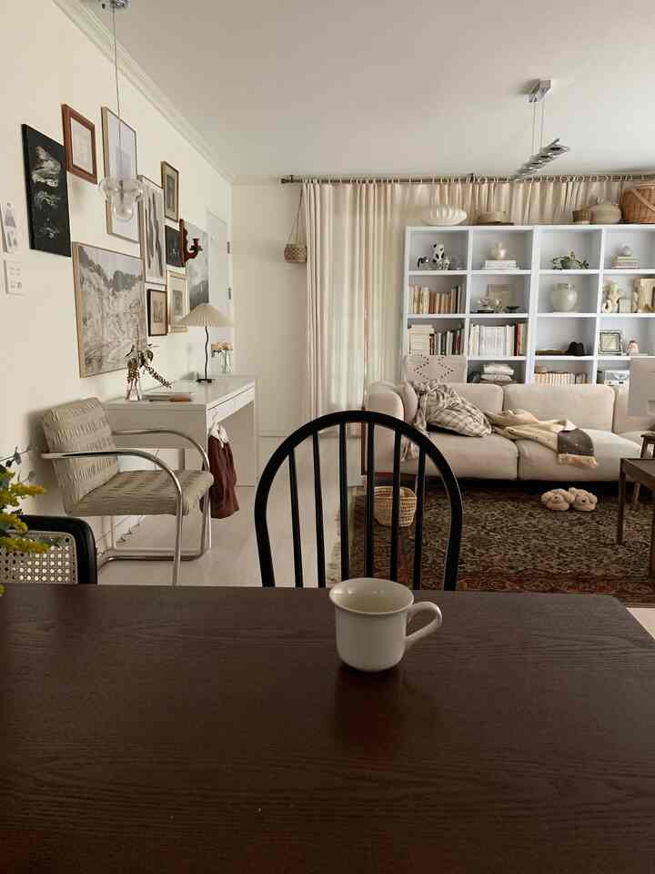 Natural beige-toned living and dining room with sofa, bookshelf, and wooden dining table creating a warm atmosphere.