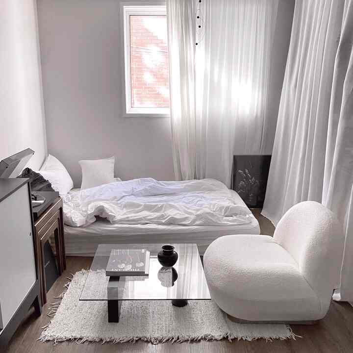 ホワイトとナチュラルトーンが調和したワンルーム寝室、モダンなチェアとガラスのコーヒーテーブルが配置されたシンプルで落ち着いたインテリア