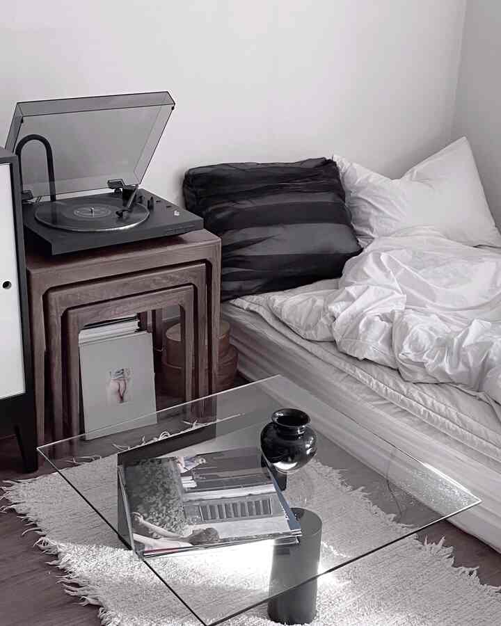 A white and black toned bedroom featuring a modern transparent coffee table and wooden nesting tables in a minimalist space