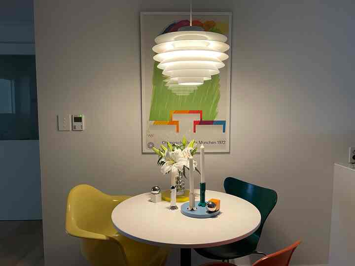 Modern kitchen with white walls and round dining table, featuring colorful chairs and a layered pendant light creating a bright atmosphere