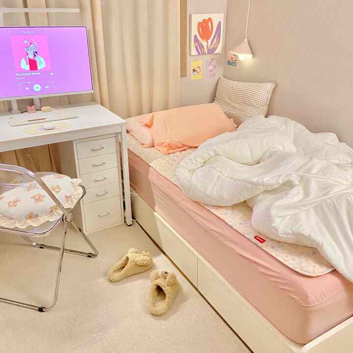 白とピンクの色調の寝室、コンパクトなベッドと机、かわいい電気毛布と壁の飾りが配置された雰囲気のある個室インテリア