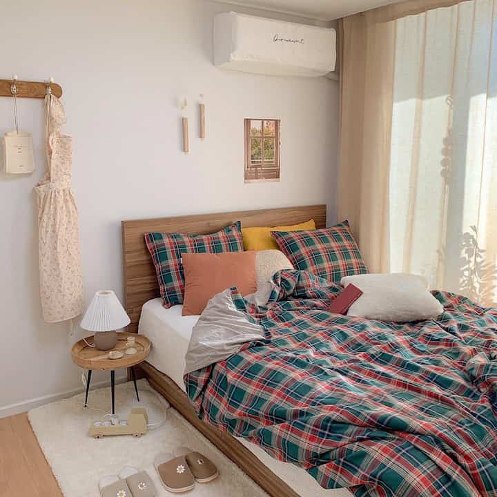 Soft white and natural wood tone bedroom featuring green check autumn bedding and cushions creating a cozy atmosphere
