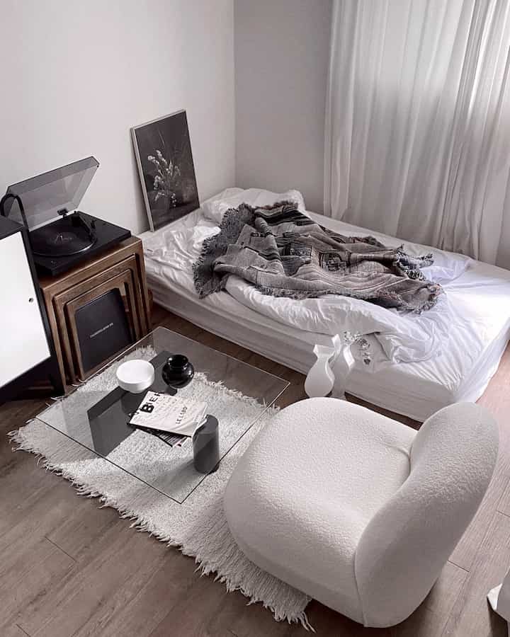 Soft white and gray toned studio bedroom featuring a low bed and turntable in a modern, cozy setting