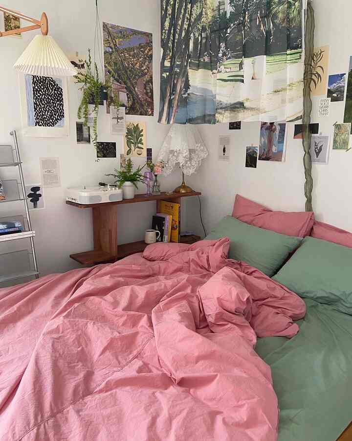 A cozy studio bedroom in pink and green tones featuring plants and posters
