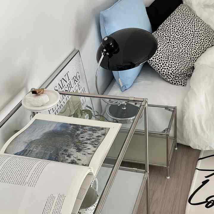 A white and black toned bedroom featuring glass nightstand and assorted pillows creating a cozy atmosphere