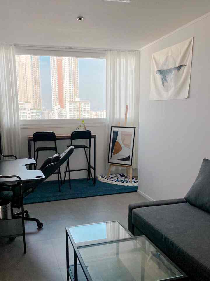 A compact white and gray toned home office and gaming room featuring a desk by the window and a corner sofa bed creating a clean atmosphere