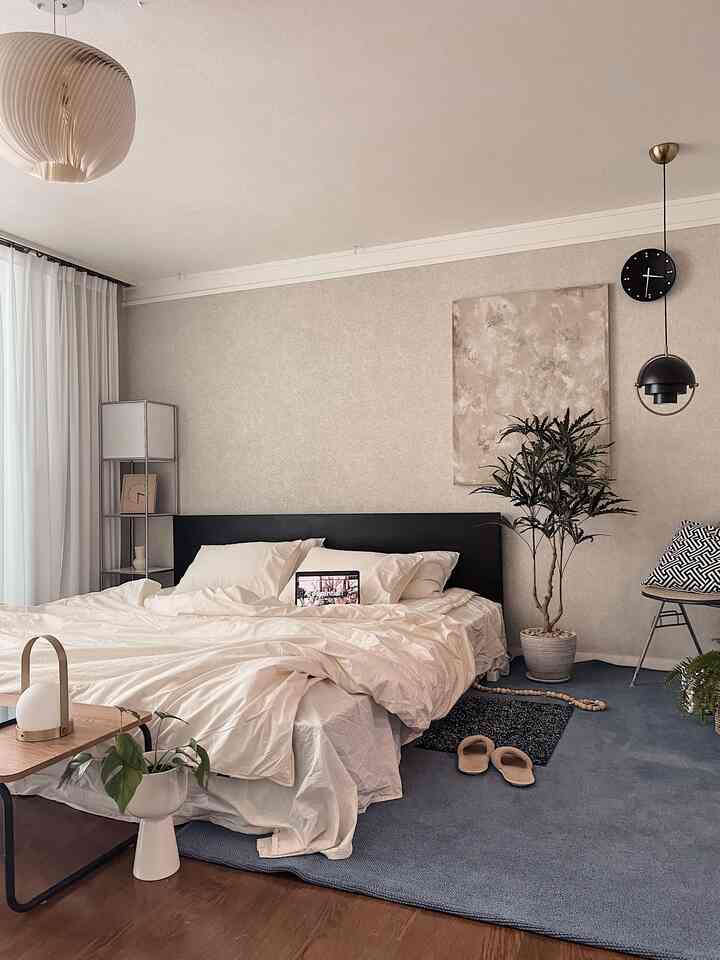 ベージュ色の壁と白い寝具が配置された寝室、青いラグと複数の照明が印象的なモダンで自然なインテリア