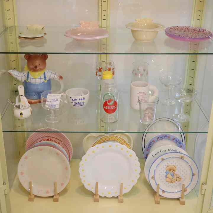 黄色調のキッチン用飾り棚にヴィンテージの熊モチーフの食器やプレート、グラスが配置された雰囲気のあるインテリア