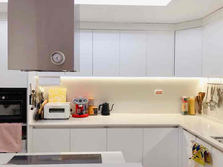 明るく清潔感のあるホワイトトーンのキッチン、上下のキャビネットと調理台、電気ポットやコーヒーマシンが配置されたモダンでミニマルな空間