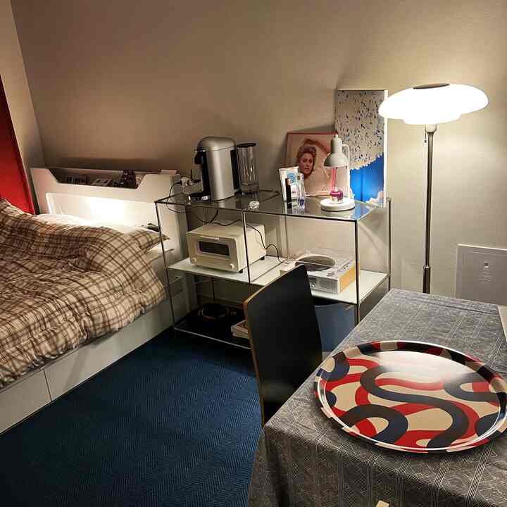 A white and black-toned studio apartment bedroom-living room featuring checkered bedding and a floor lamp, creating a cozy atmosphere
