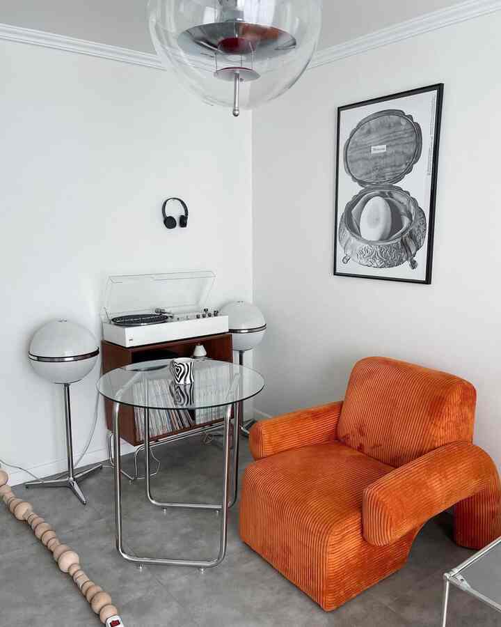 Bright white and orange toned living room featuring transparent glass table and vibrant orange armchair in a modern setting