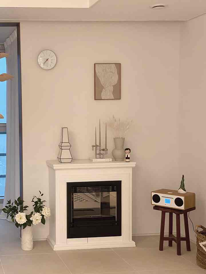A natural-toned living room featuring a fireplace and a wood stool with a Bluetooth speaker, creating a neat and warm ambiance