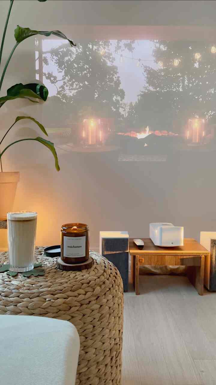 Natural wood tones and rattan decor in a small home cafe space, featuring candle and projector video for a cozy relaxation mood