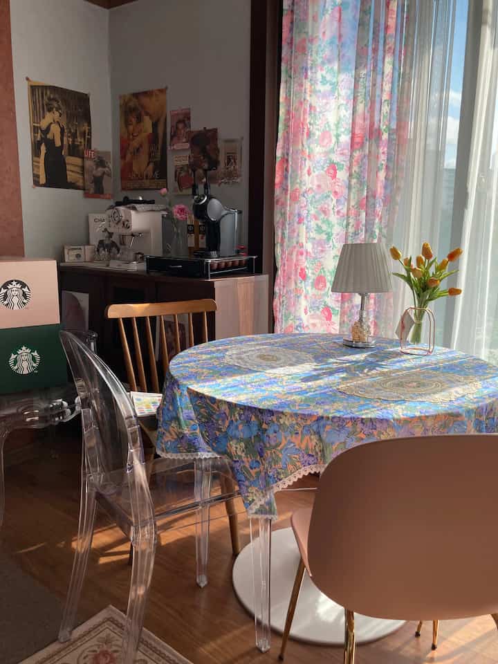 パステルとナチュラルトーンの融合したおうちカフェ空間、花柄テーブルクロスとヴィンテージポスターが印象的な居心地のよいリビング