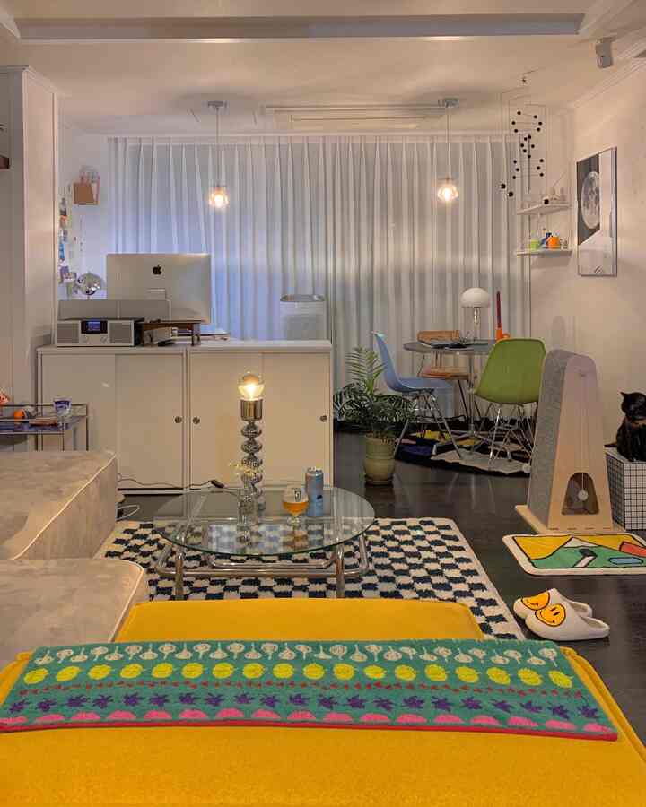 Bright modern living room with a central checkerboard rug and transparent glass table, cozy interior featuring a cat and a cat tower on the right