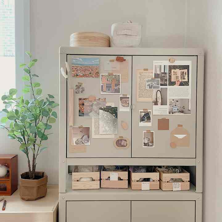 柔らかなベージュとグレーのトーンのワークスペースキャビネット、ポストカードと壁飾りで彩られた雰囲気のある空間
