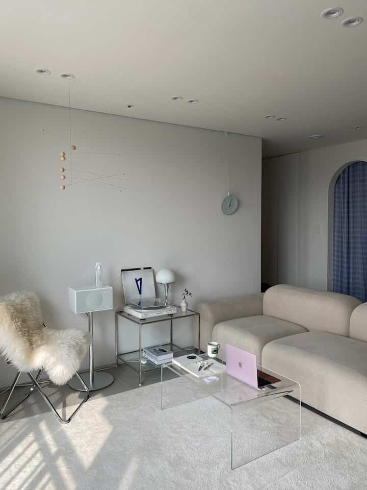 White and beige toned living room featuring a transparent acrylic table and beige modular sofa in a modern, cozy remote work space