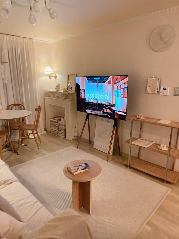 Natural beige and wood-toned living room featuring a round table, sofa, and TV stand with a calm atmosphere