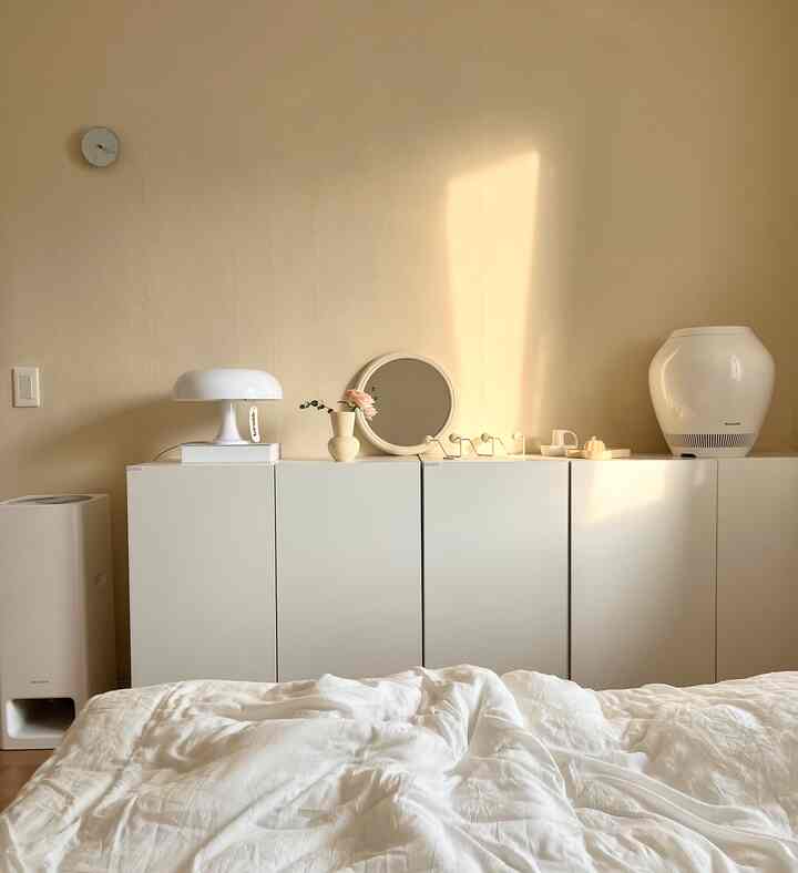 Bright and natural bedroom with warm beige walls, white cabinets, and bedding illuminated by sunlight