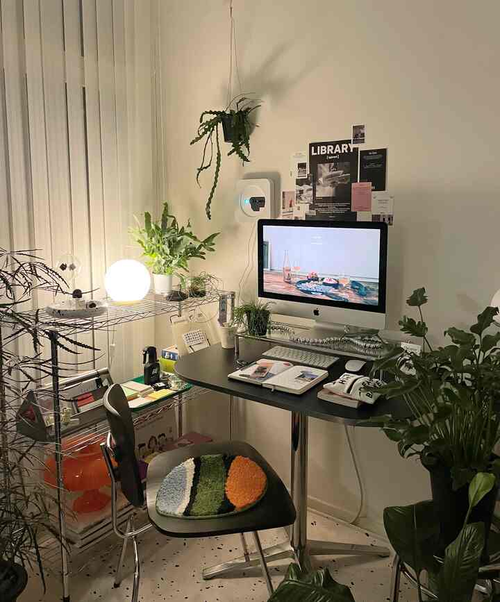 Modern compact home office with black desk and chair, decorated with various plants and a metal shelving unit