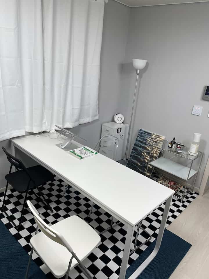 Modern studio apartment with black and white tones featuring a long desk, checkered rug, and minimalist home office setup
