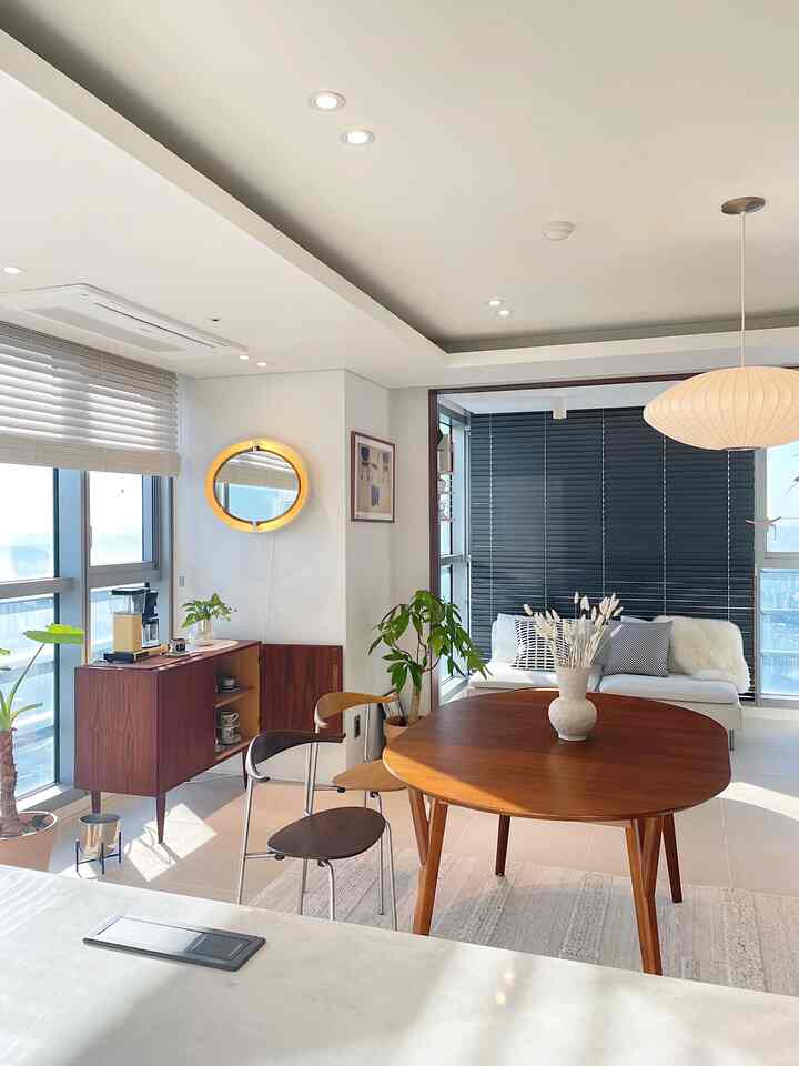 ナチュラルモダンのワンルーム、木製のダイニングテーブルやソファ、ブラインド、ペンダントライトが配置された明るく落ち着いた印象的な空間