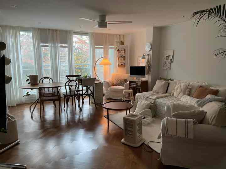 暖かみのあるブラウンの木目調の床とアイボリーのソファが配された、自然光が差し込む明るいリビングルーム